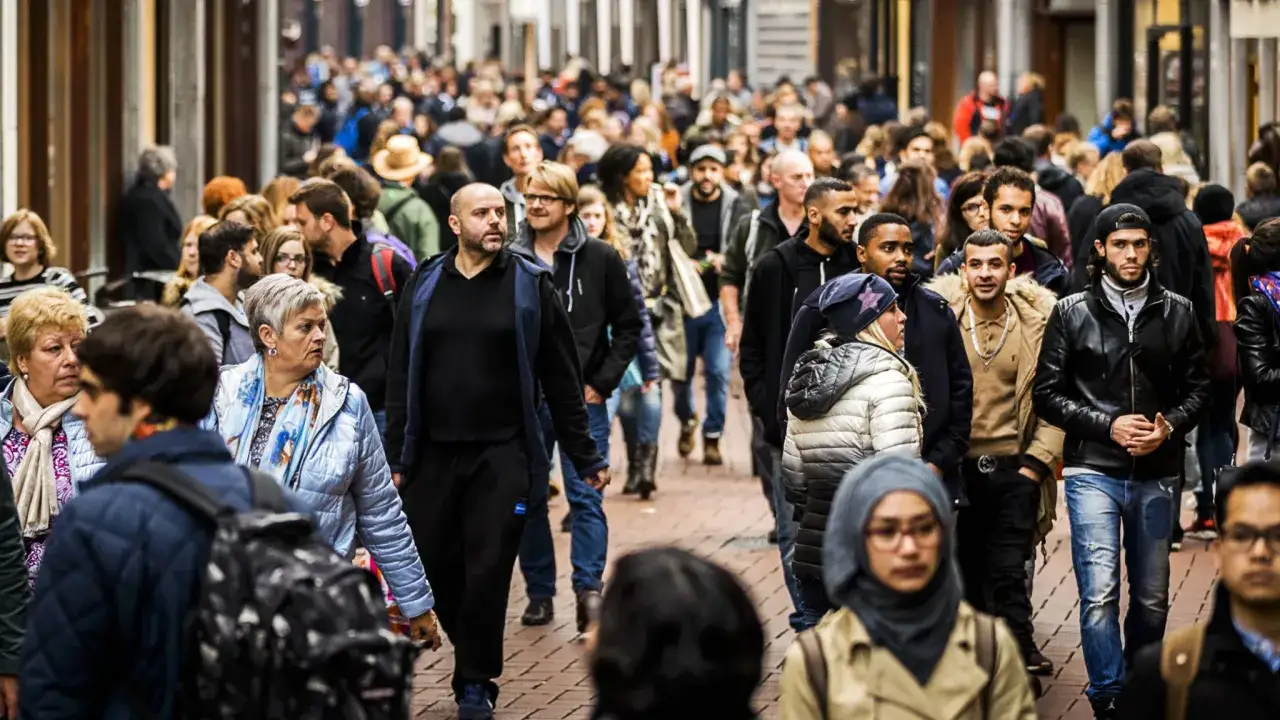 Drukte op straat met diverse mensen, waaronder tweede generatie migranten, die door een winkelstraat lopen.