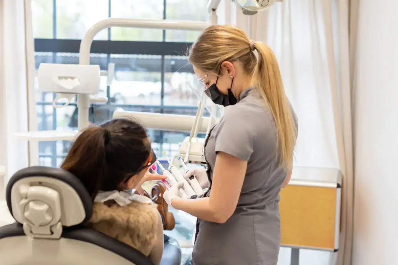 Dentystka w masce i okularach pokazuje pacjentce w ciąży narzędzia. Bezpieczne znieczulenie u dentysty w ciąży jest priorytetem.