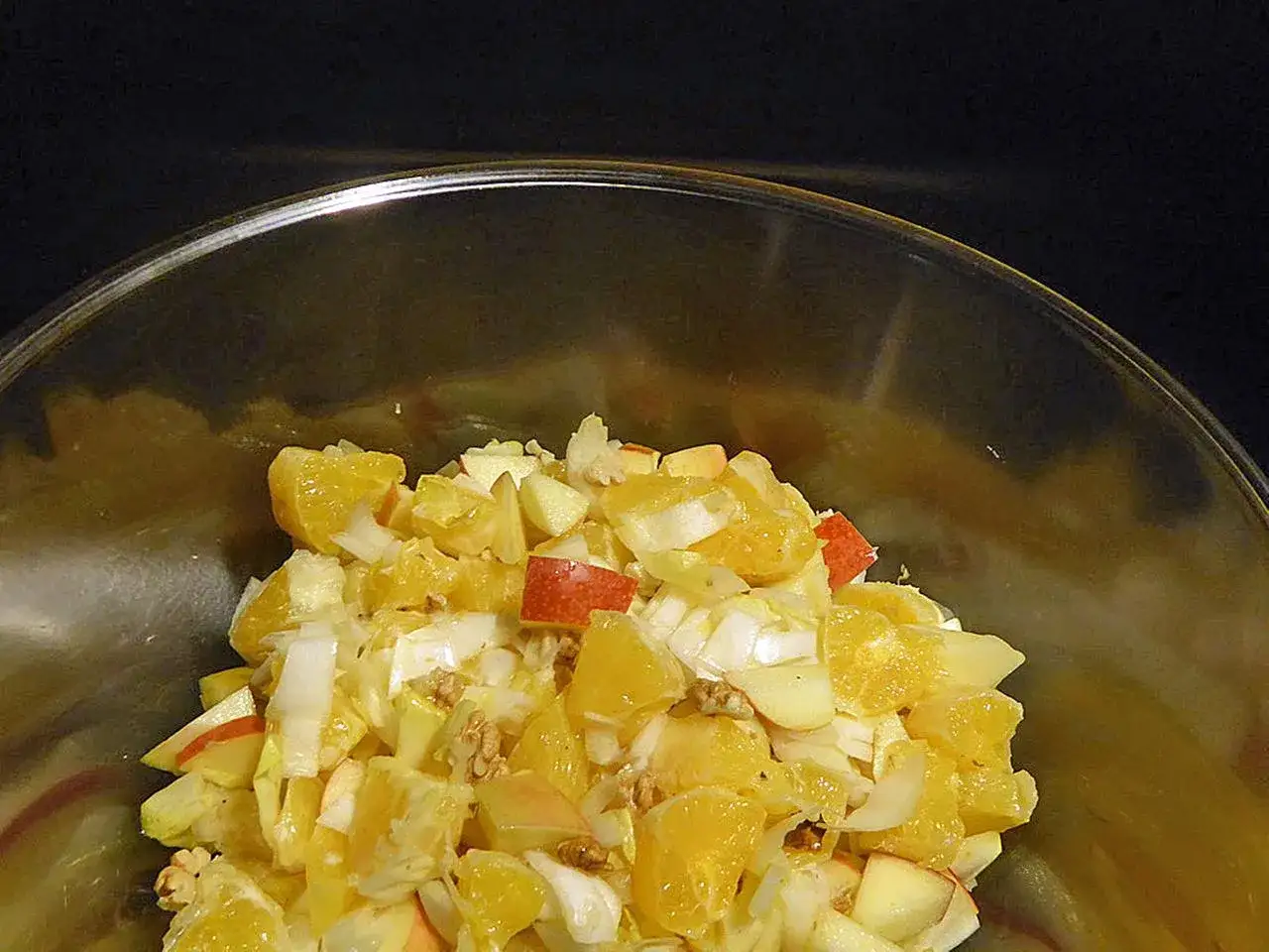 Ein erfrischender chicoree salat mit Orangenstücken, Äpfeln und Walnüssen in einer Glasschüssel.