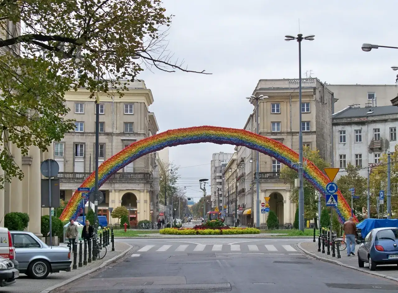 Tęcza na ulicy, symbol nadziei i r&oacute;żnorodności, rozciąga się nad skrzyżowaniem.