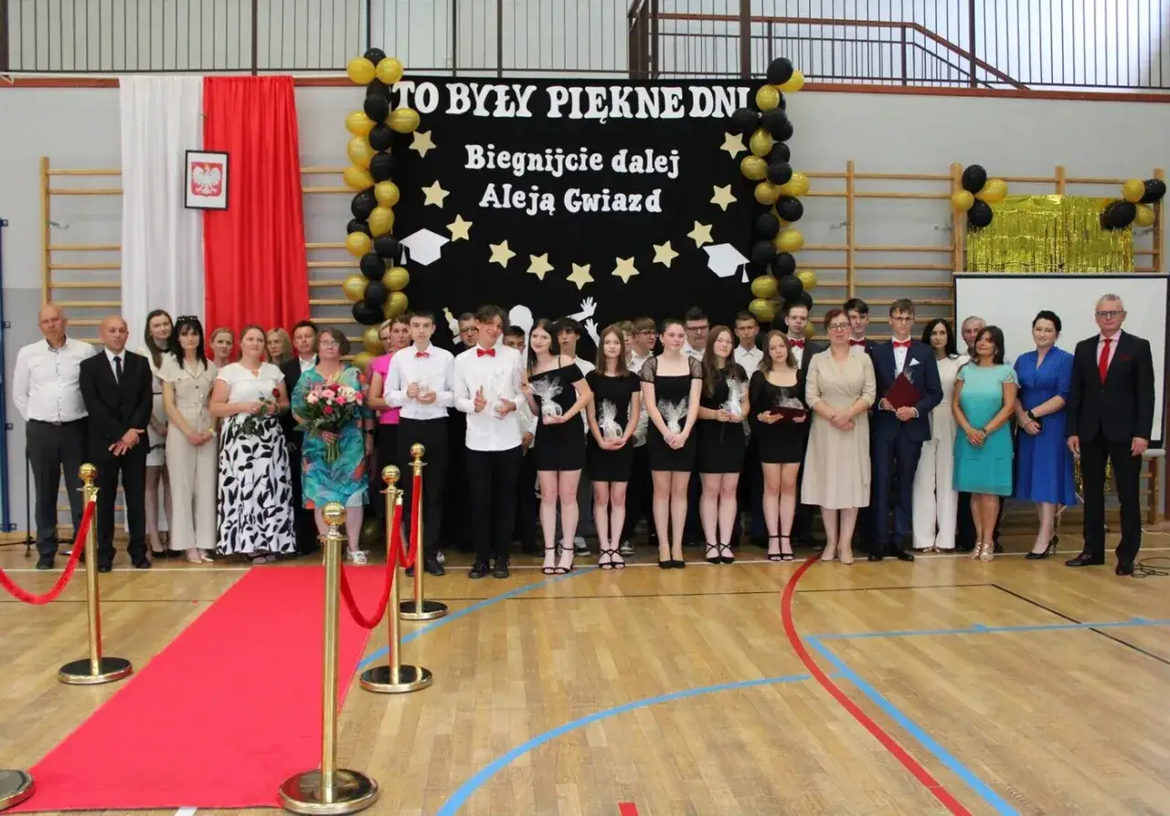 Uczniowie i nauczyciele świętują zakończenie roku szkolnego. Na scenie baner z napisem 
