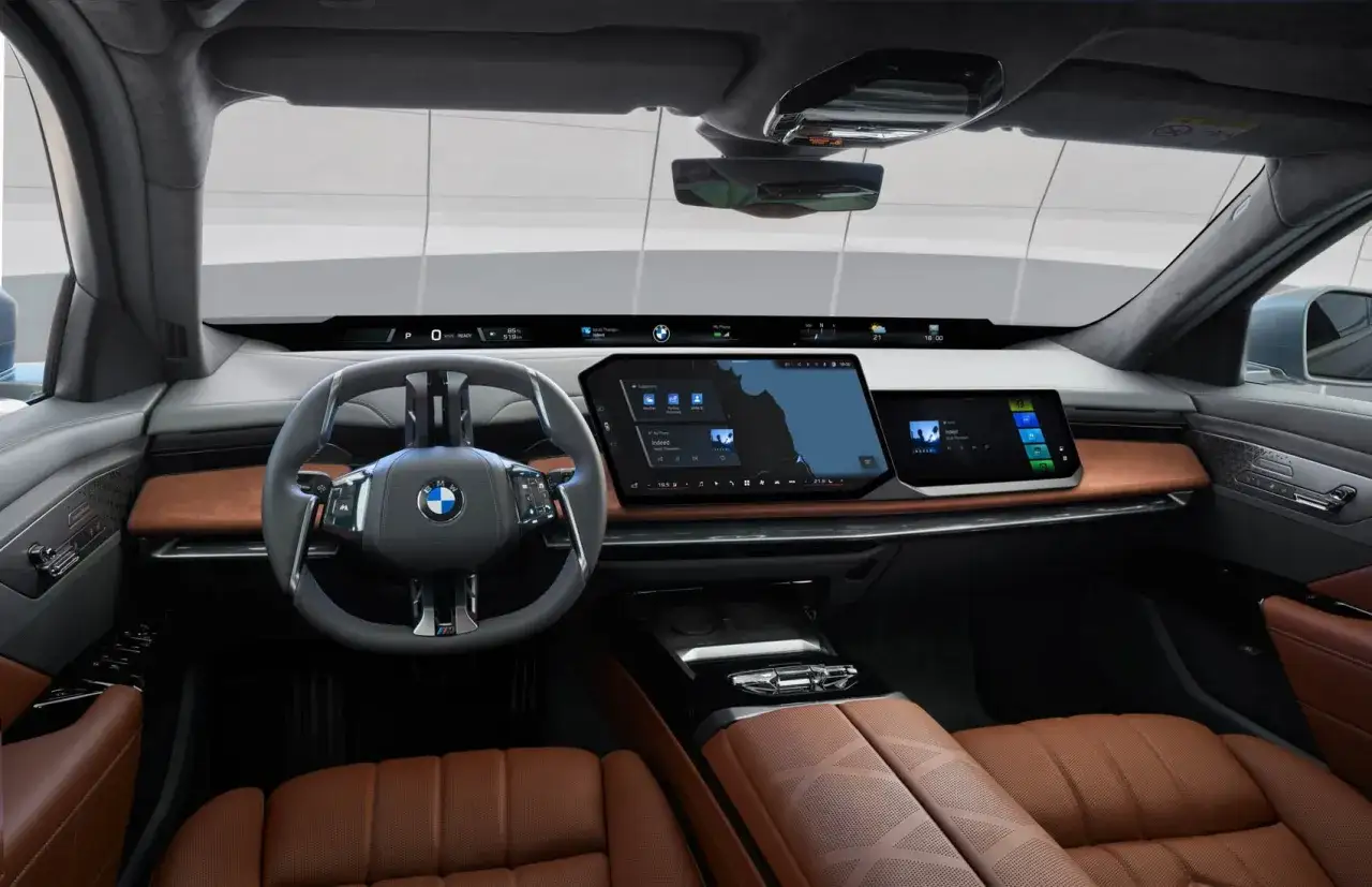 Wnętrze BMW M7 z nowoczesnym kokpitem, dużymi ekranami i brązową skórzaną tapicerką.