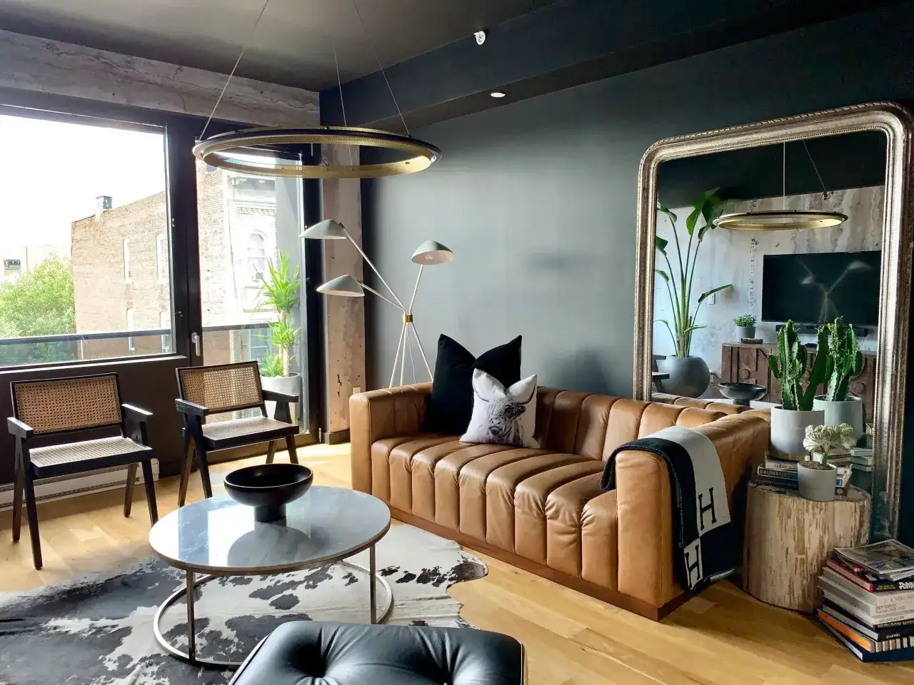 Ideas for how to decorate around a large wall mirror: a plush leather sofa, plants, and a stack of books create a cozy vignette.