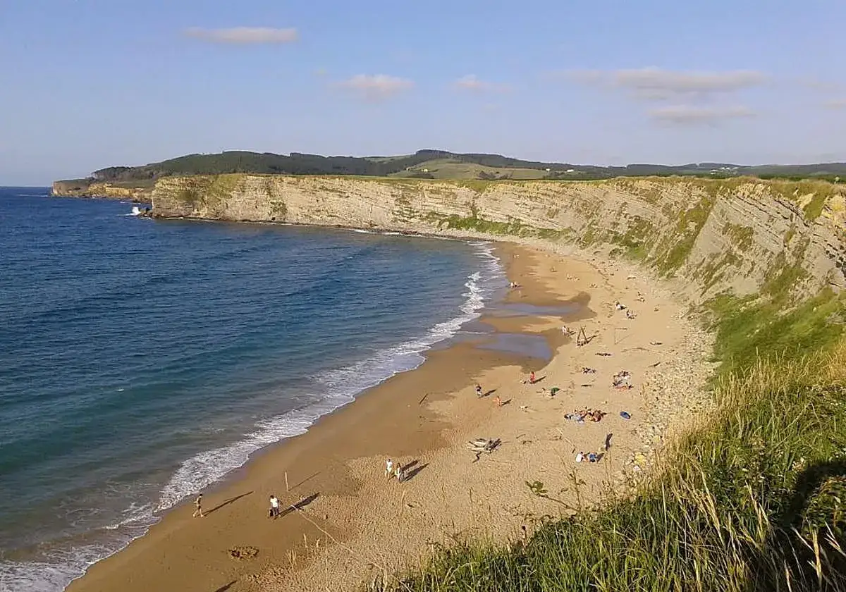 La **playa de cerrias** se extiende bajo acantilados imponentes. El mar azul baña la arena dorada, salpicada de bañistas disfrutando del sol.