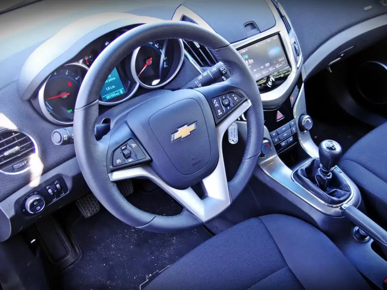 Wnętrze Chevroleta Cruze. Kierownica, deska rozdzielcza z radiem i ekranem, dźwignia zmiany biegów. Wiele osób szuka chevrolet cruze opinie przed zakupem.