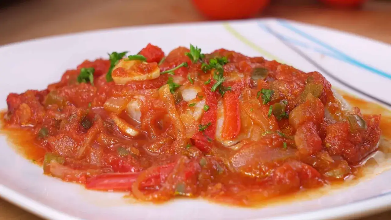 Delicioso bacalao con tomate, pimientos y cebolla, adornado con perejil fresco. Un plato lleno de sabor.