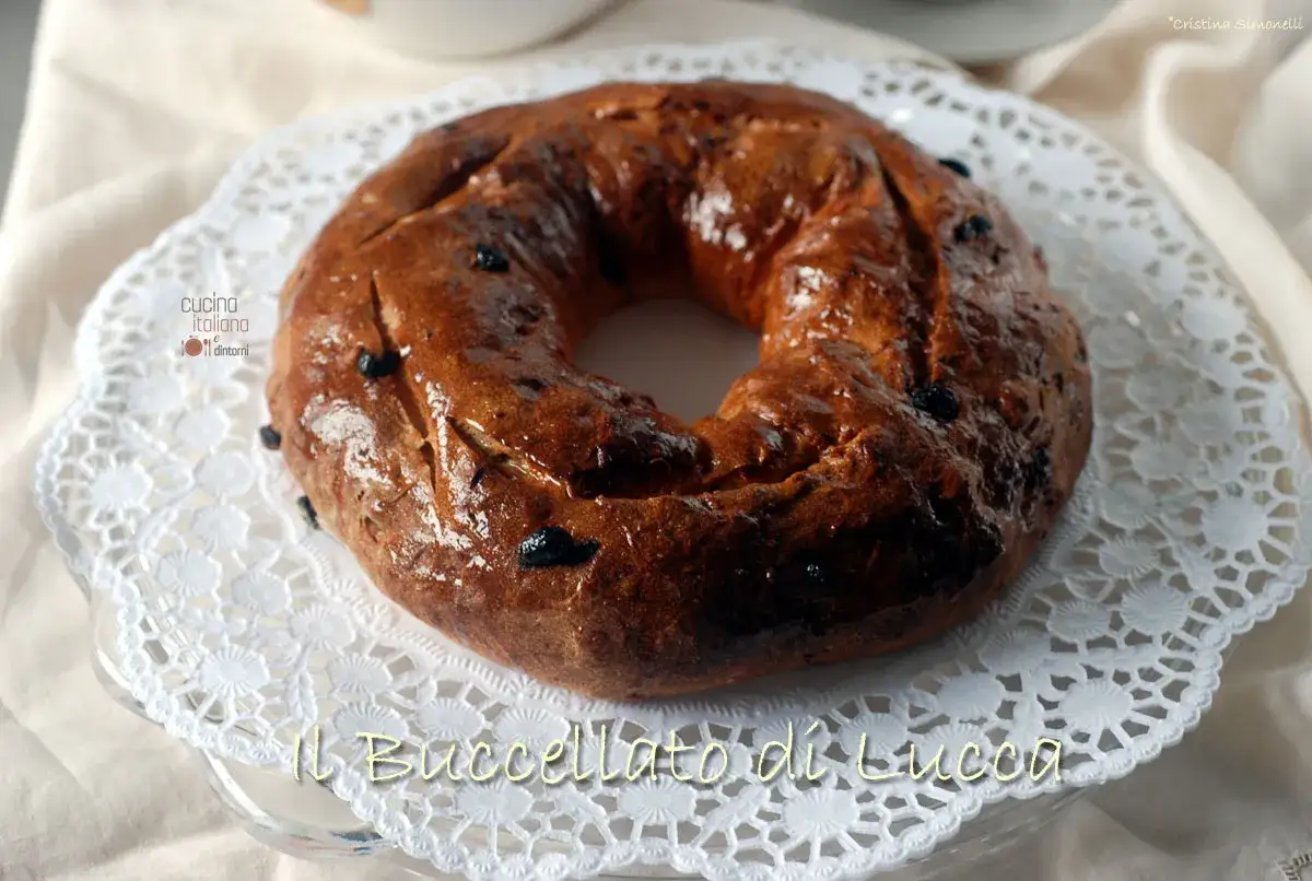 Il Buccellato di Lucca, un dolce tradizionale lucchese, &egrave; un pane dolce a forma di ciambella con uvetta, servito su un centrino di pizzo.