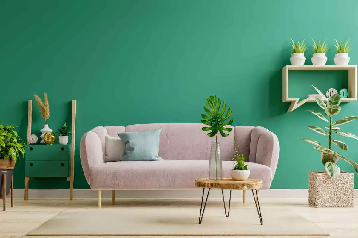 Soggiorno con divano rosa cipria e parete verde petrolio. Un tavolino in legno grezzo e piante creano idee pareti colorate particolari.