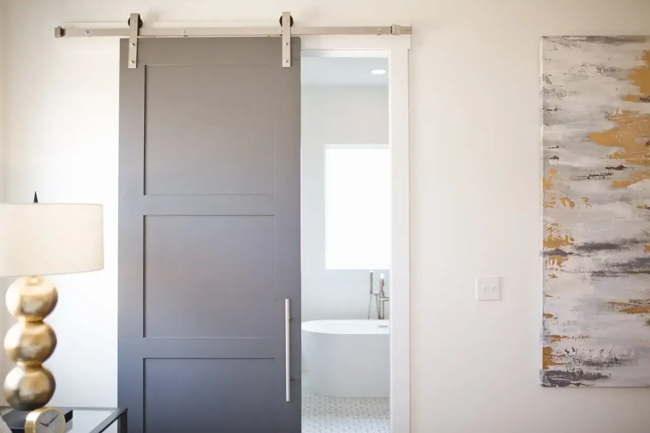 Puerta corredera gris moderna, ideal para instalar en ba&ntilde;os o habitaciones. El sistema de riel plateado es visible.
