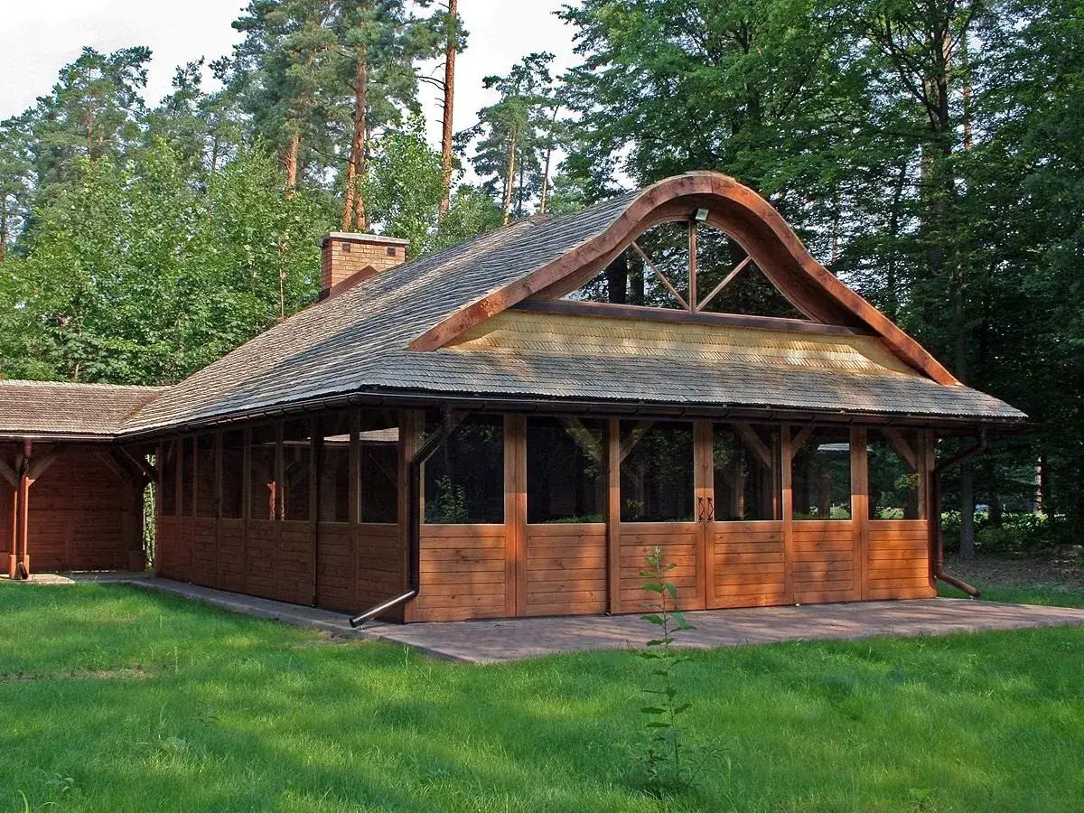 Drewniana altana w Sękocinie z charakterystycznym, falistym dachem i przeszklonymi ścianami, otoczona zielenią.