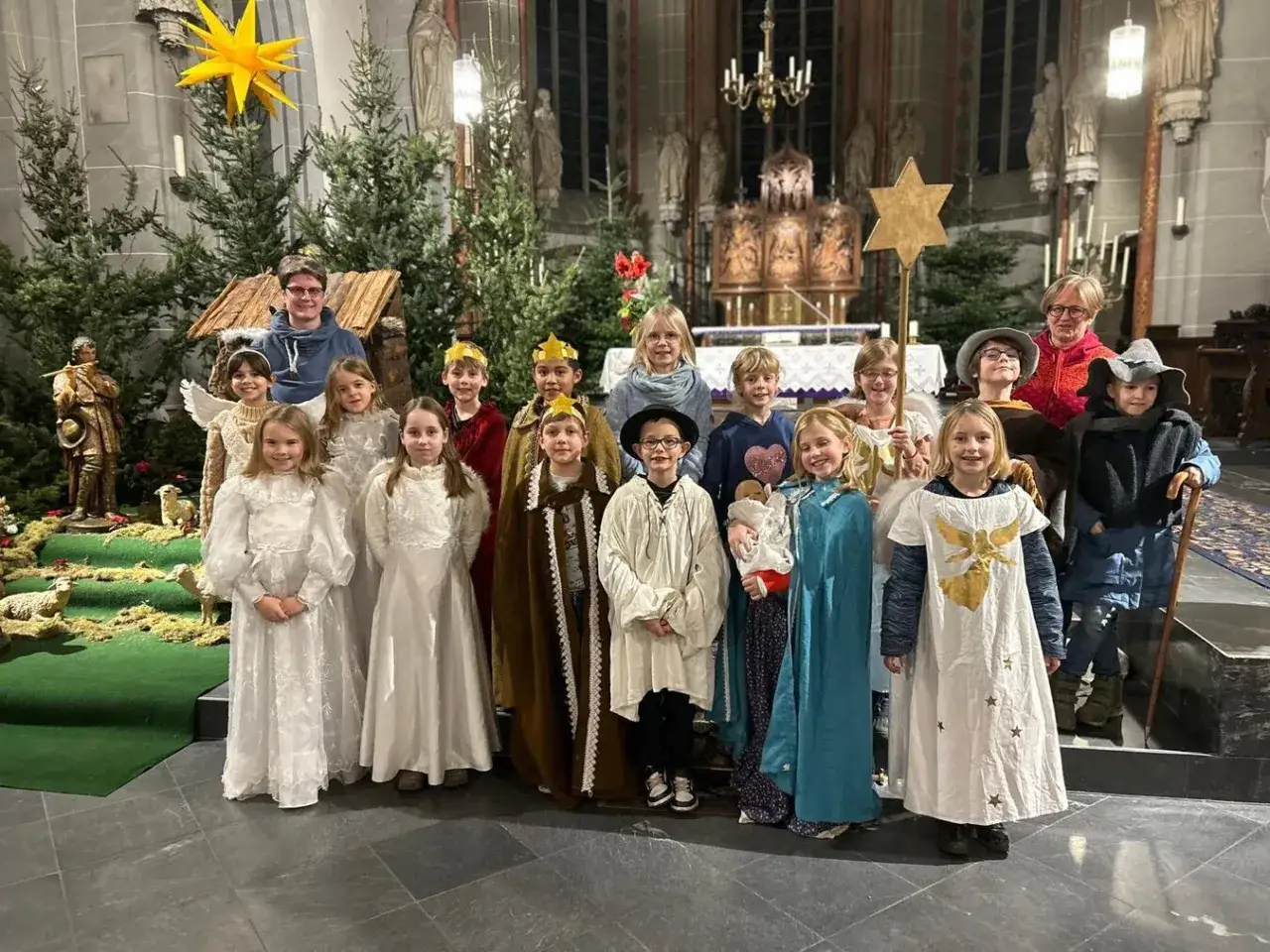 Kinder in Kost&uuml;men, die eine Weihnachtsgeschichte f&uuml;r den Gottesdienst am Heiligen Abend auff&uuml;hren, stehen vor einer Krippe und Weihnachtsb&auml;umen.