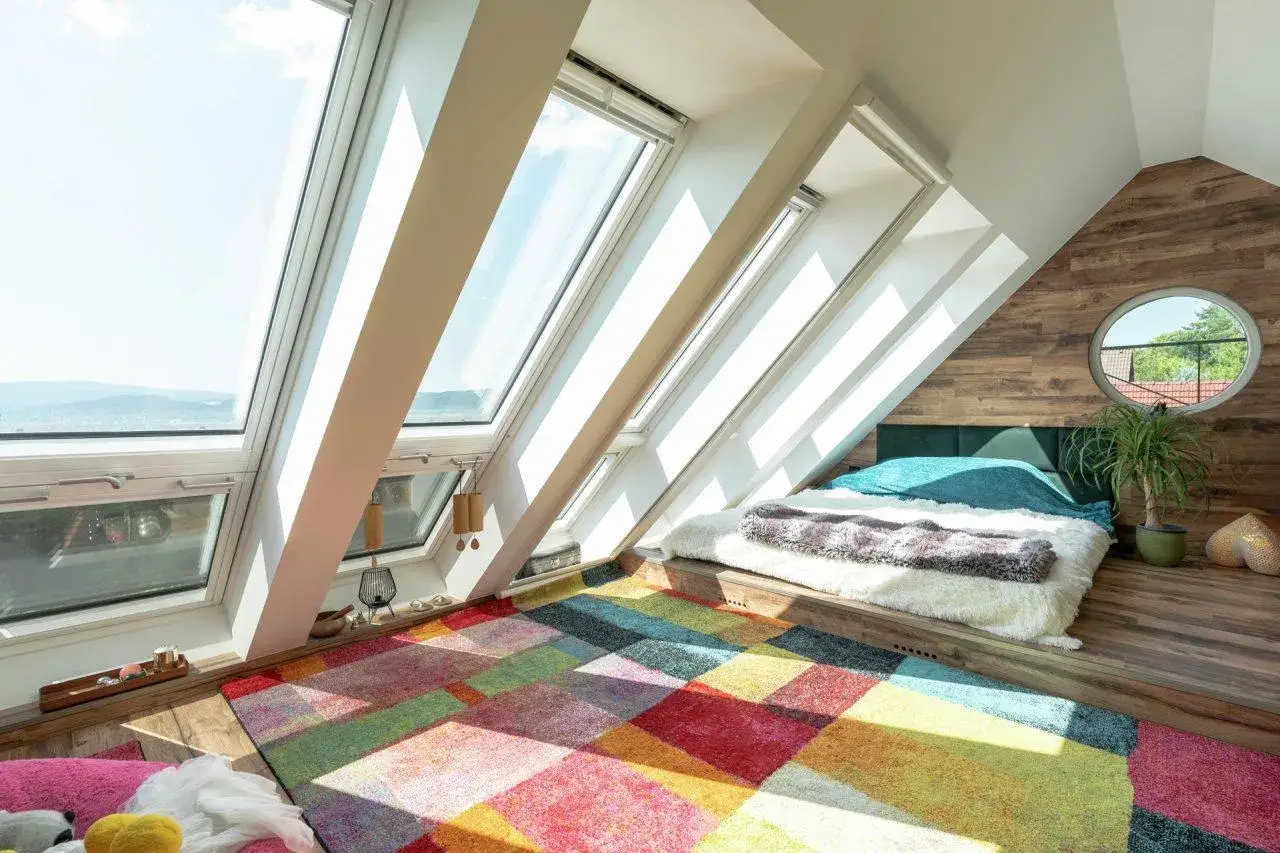 Accogliente camera da letto in soffitta, con lucernari luminosi, un letto comodo e un tappeto colorato. La soffitta, in questo caso, ha un significato di spazio intimo e creativo.