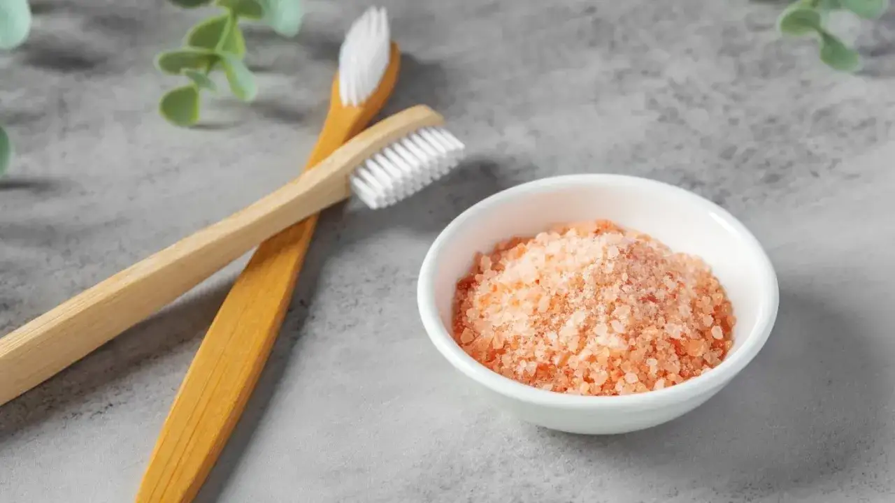 Zwei Bambuszahnb&uuml;rsten und eine Schale mit rosa Kristallsalz, ideal zur Linderung von zahnfleisch schmerzen.