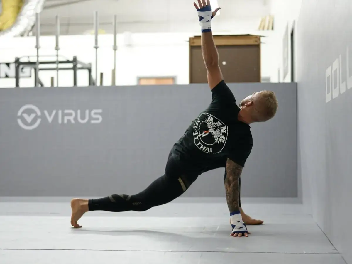 Un athlète de mma sport de combat s'étire dans une salle d'entraînement, le bras levé, le corps en torsion.
