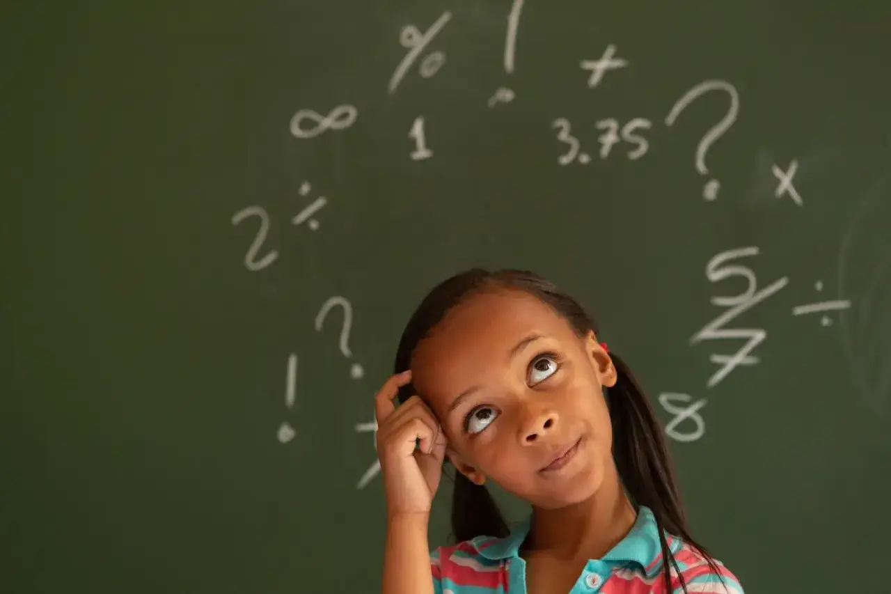 Ni&ntilde;a pensativa frente a un pizarr&oacute;n con s&iacute;mbolos matem&aacute;ticos, &iquest;qu&eacute; es la discalculia?