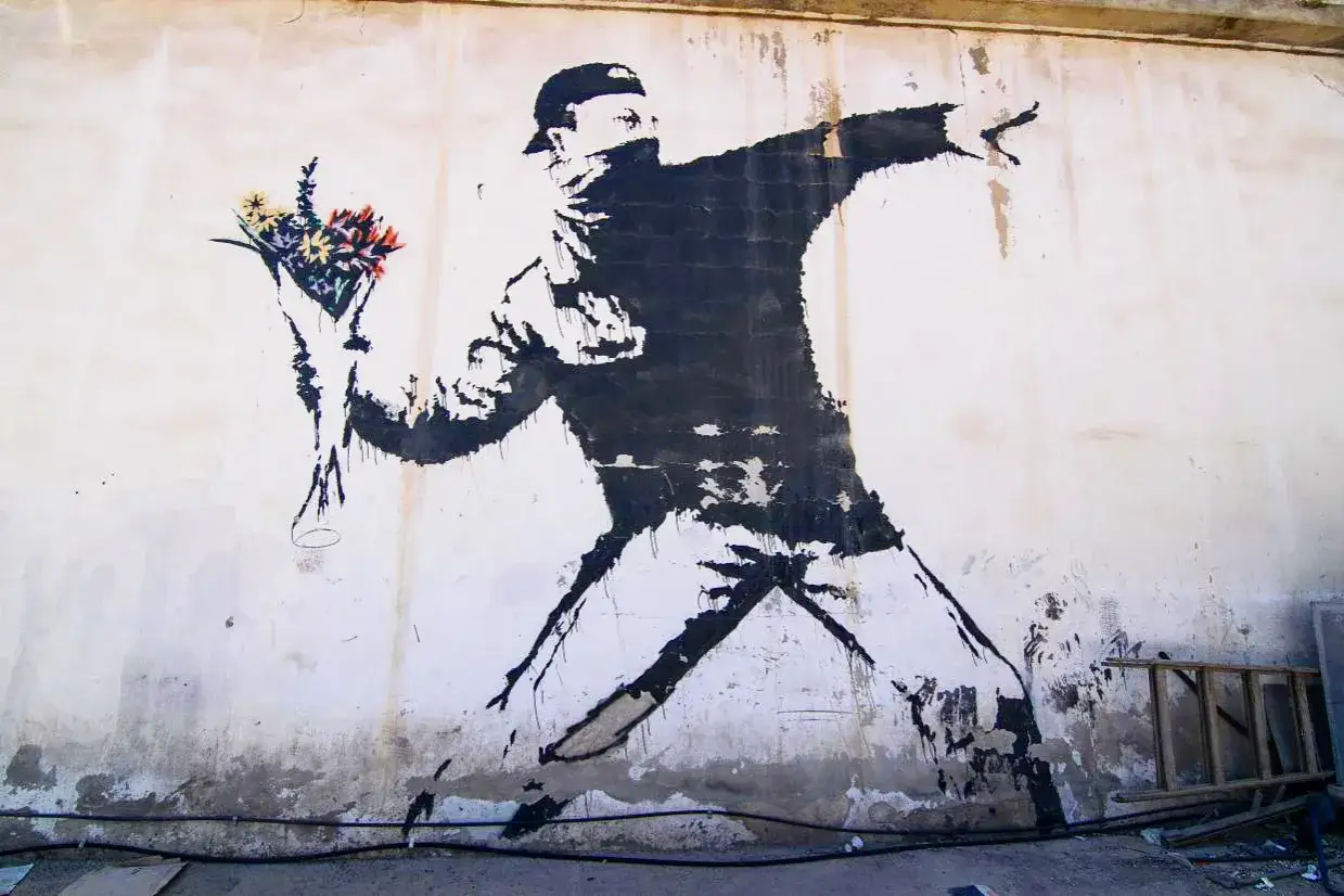 Une oeuvre de Banksy : un homme lance un bouquet de fleurs, son visage masqu&eacute;, sur un mur d&eacute;cr&eacute;pit.