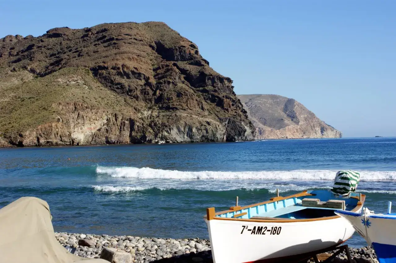 Barco en la playa con el imponente cerro negro almeriense de fondo y el mar azul.
