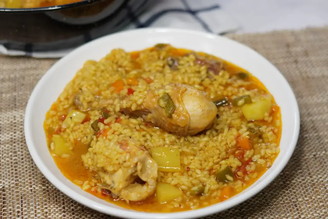 Un delicioso arroz caldoso con pollo, trozos de patata y pimientos verdes en un plato blanco.