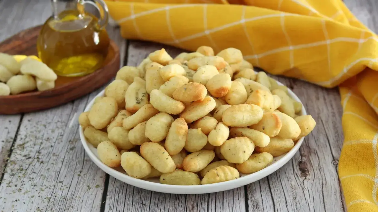 Gnocchi dorati e croccanti, cotti in friggitrice ad aria, conditi con erbe aromatiche. Accanto, olio d'oliva e gnocchi crudi.