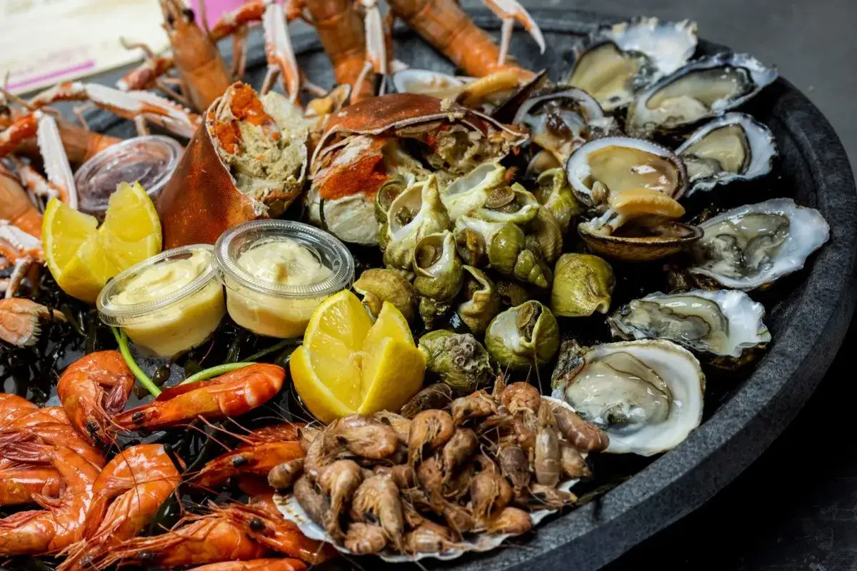 Plateau de fruits de mer frais, prêt pour la cuisson. Crevettes, langoustines, huîtres, bulots et pinces de crabe, accompagnés de citrons et de sauces.