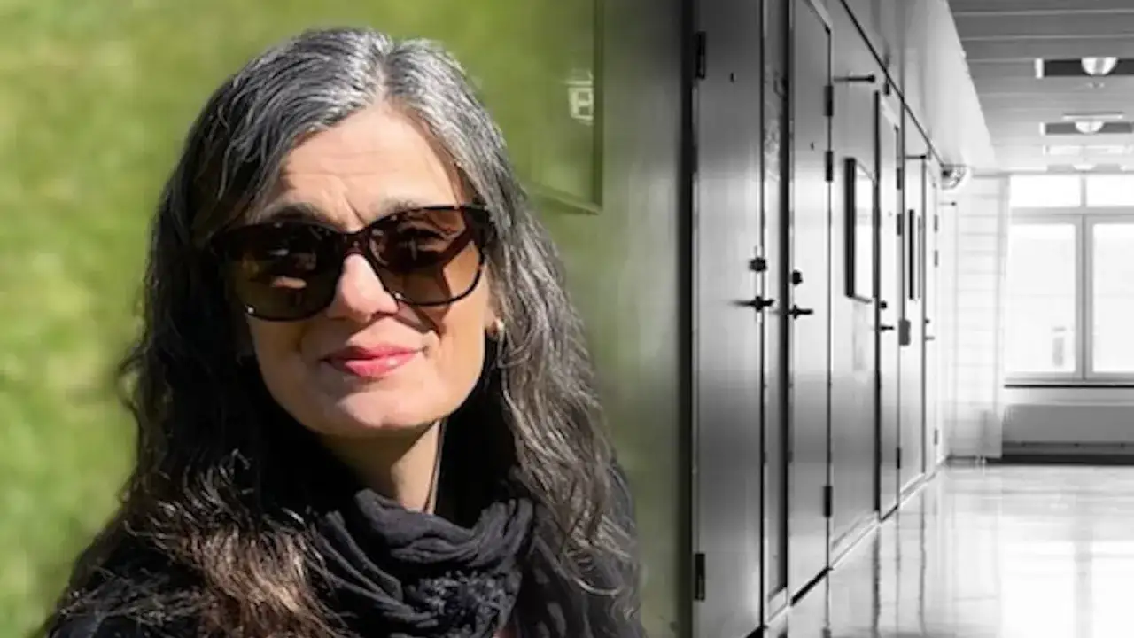 Elisabeth Punzi, med solglas&ouml;gon och gr&aring;tt h&aring;r, st&aring;r framf&ouml;r en korridor med cell-liknande d&ouml;rrar.
