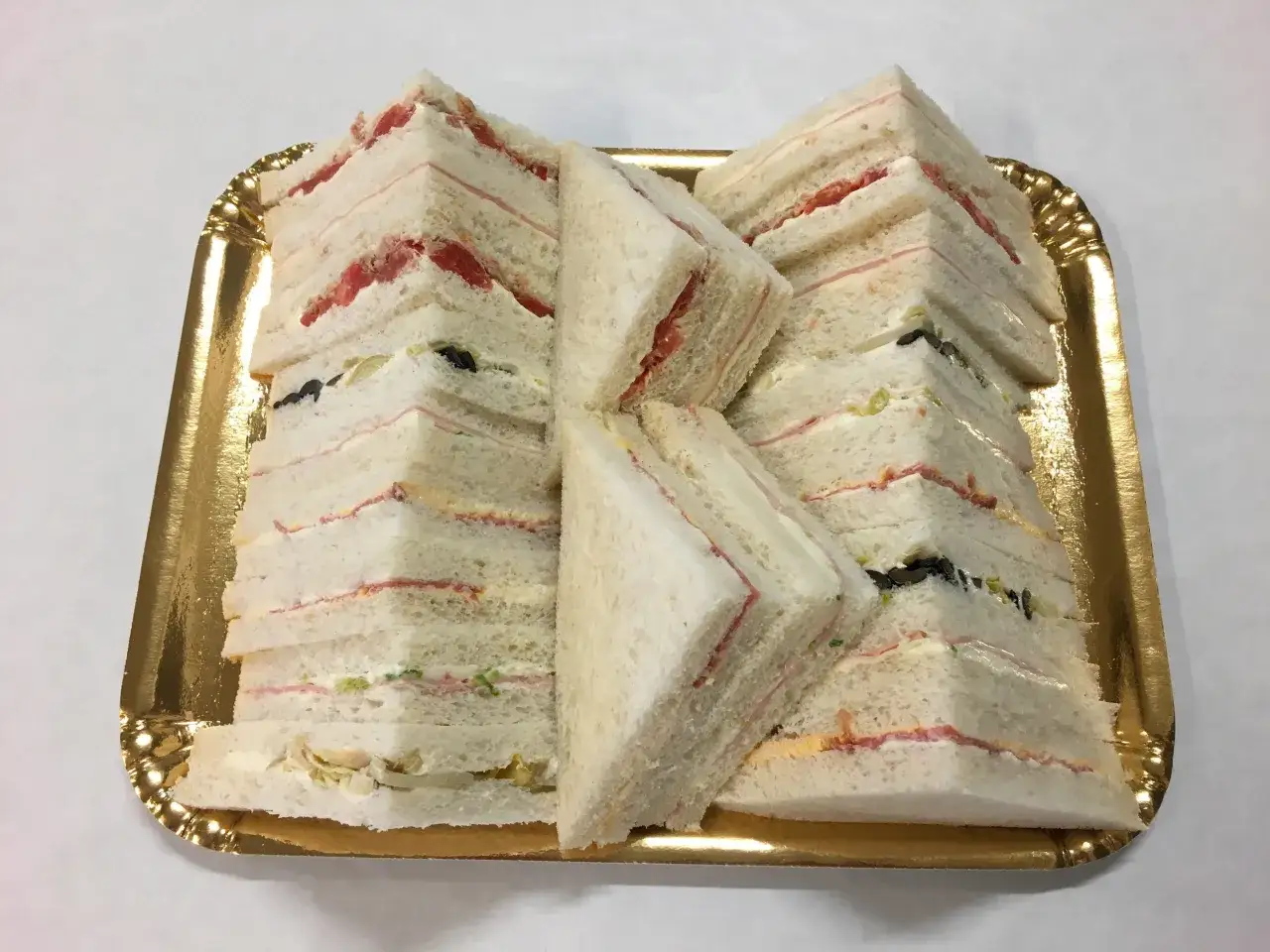 Vassoio dorato pieno di tramezzini a triangolo, con varie idee gusti e ripieni visibili, pronti per un buffet.