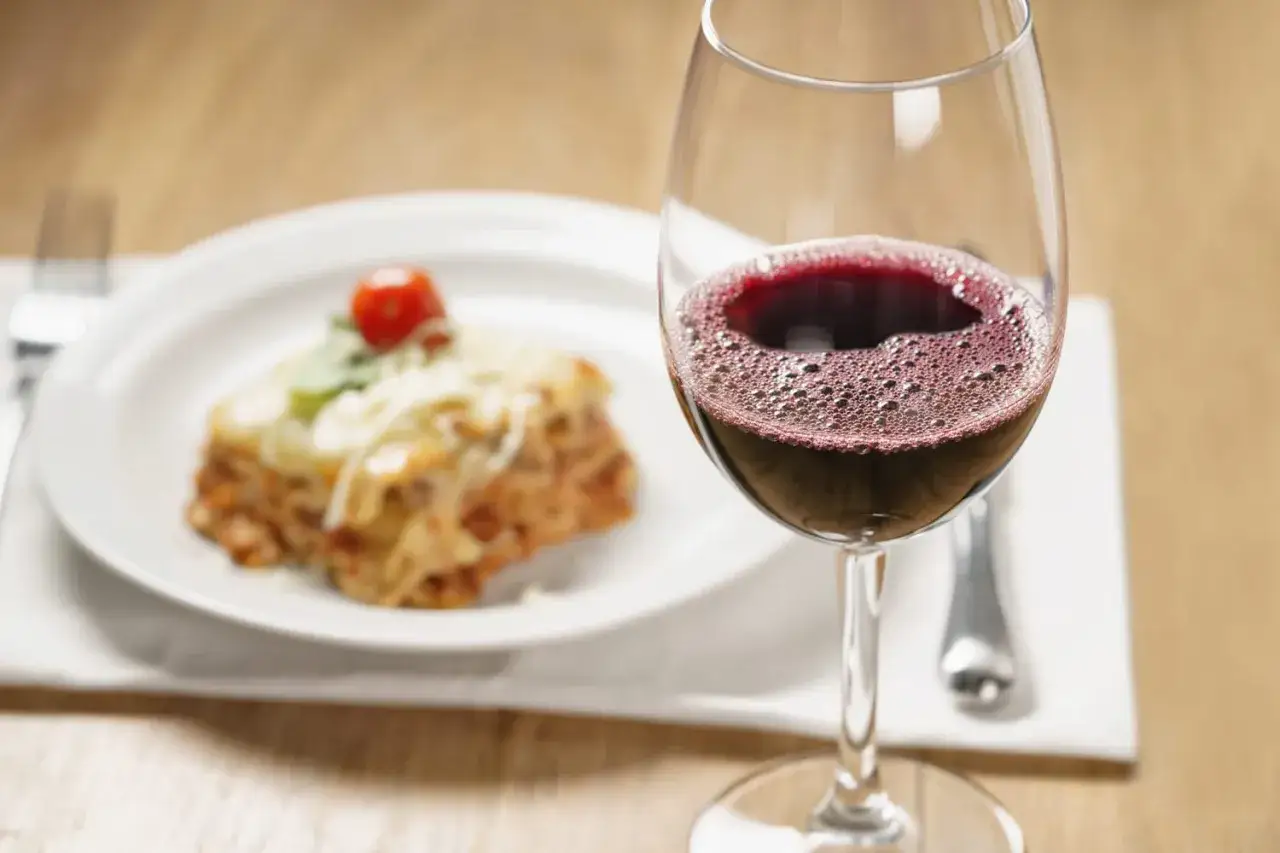 Un verre de vin rouge pétillant à côté d'une part de lasagnes savoureuse. La question est : quel vin avec des lasagnes pour un repas parfait ?