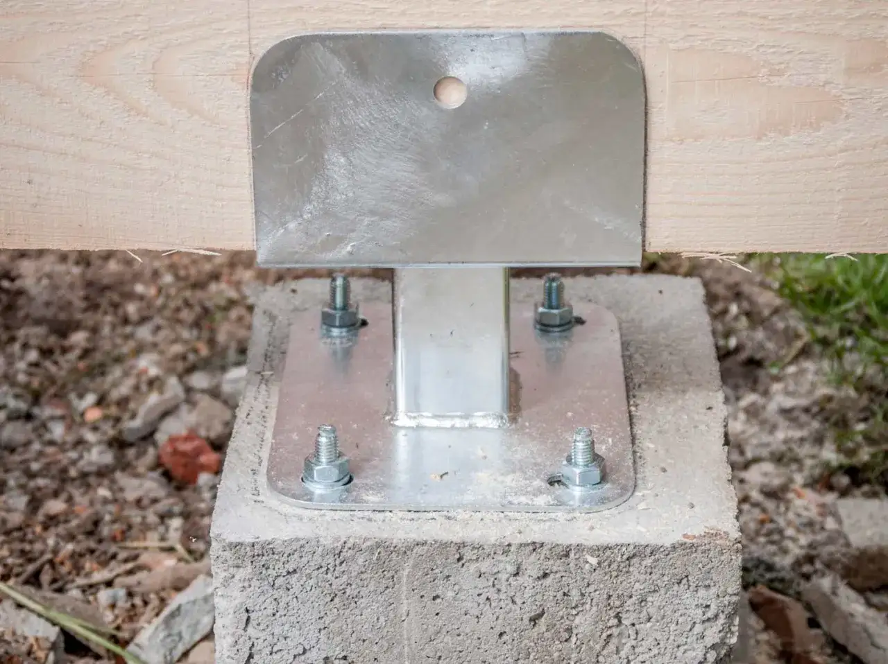 Pied de poteau métallique fixé sur un plot béton à enterrer, supportant une poutre en bois.