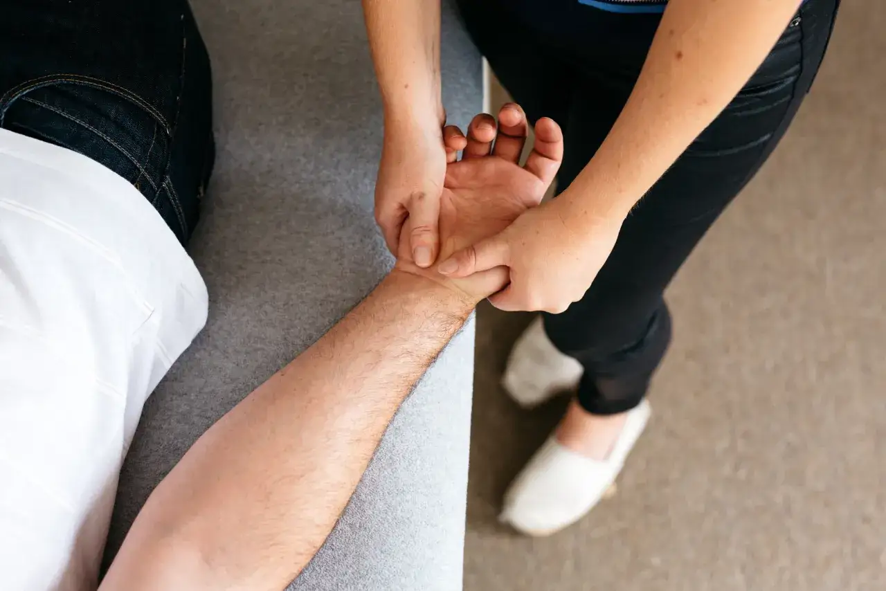 Hände einer Osteopathin behandeln den Unterarm und die Hand eines Mannes. Sie fragt sich: