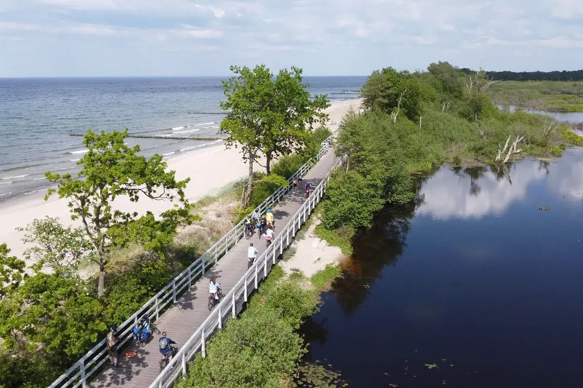 Ścieżka rowerowa wzdłuż plaży i jeziora. Ludzie cieszą się piękną pogodą, korzystając z rozwiniętej infrastruktury rowerowej.