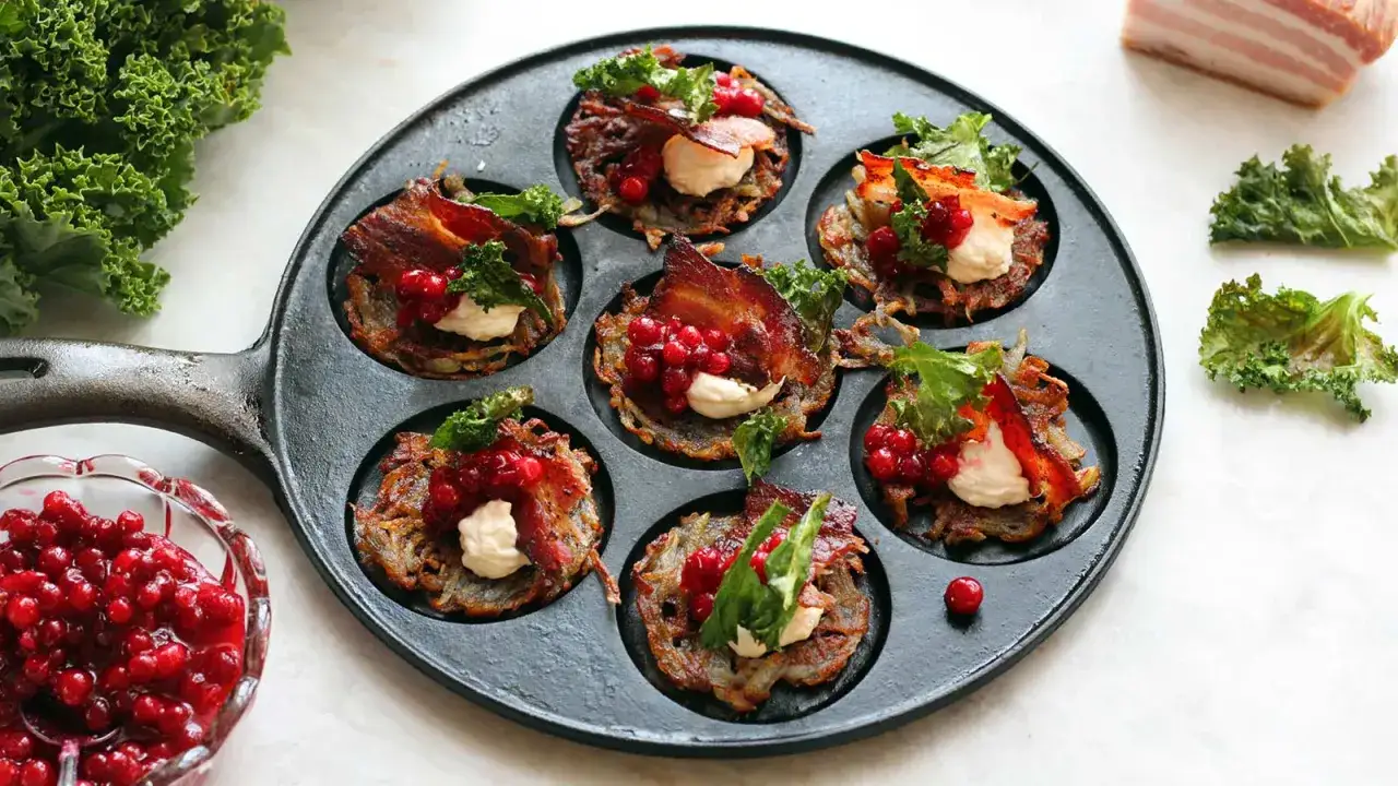 Små, gyllene rårakor i gjutjärnspanna, toppade med krämig ost, knaprigt bacon, lingon och grönkål. Ett härligt råraka recept för fest eller vardag.