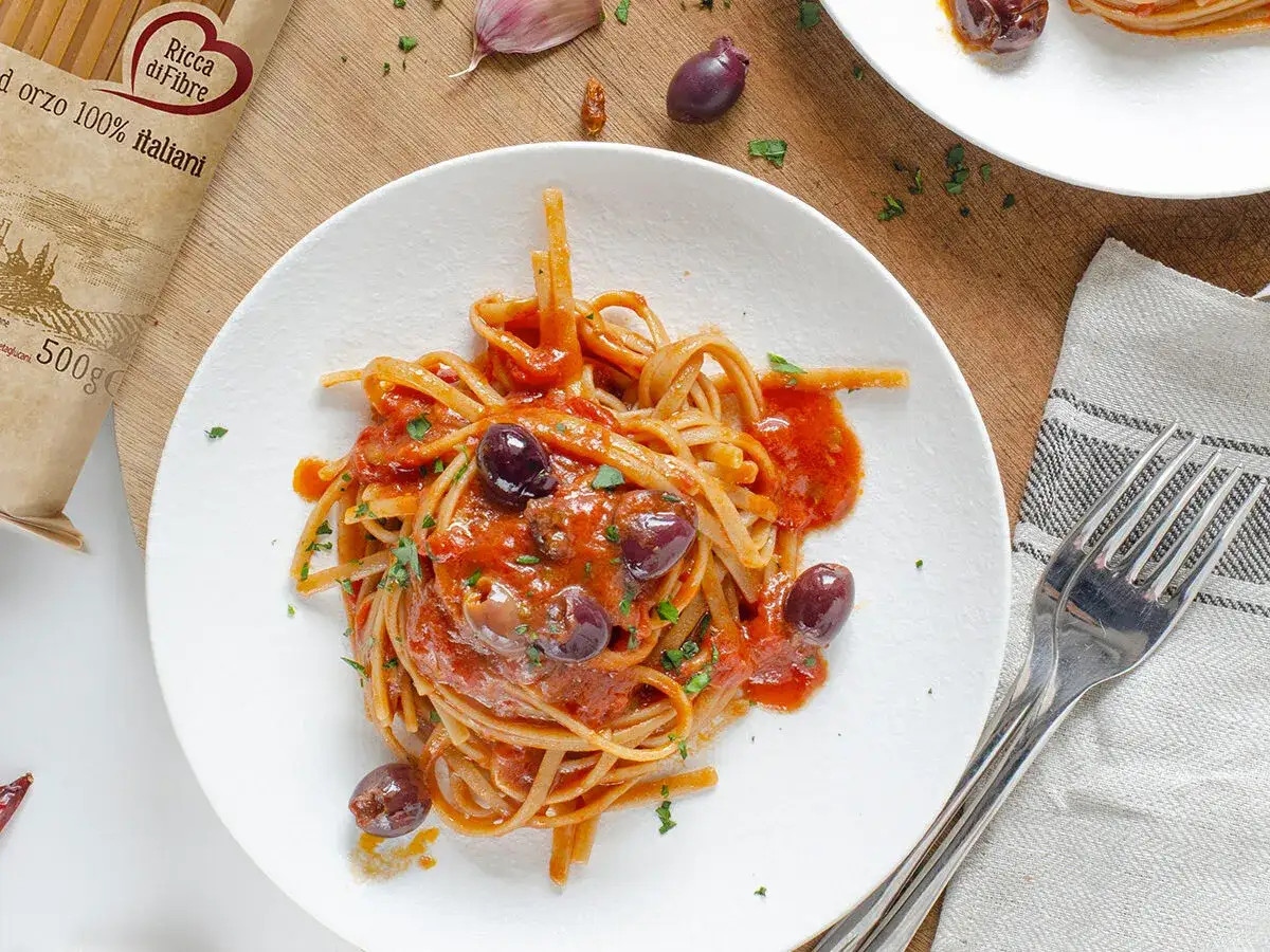 Un piatto di linguine con sugo rosso, olive nere e prezzemolo. Un assaggio di pasta alla puttanesca, pronto per essere gustato.
