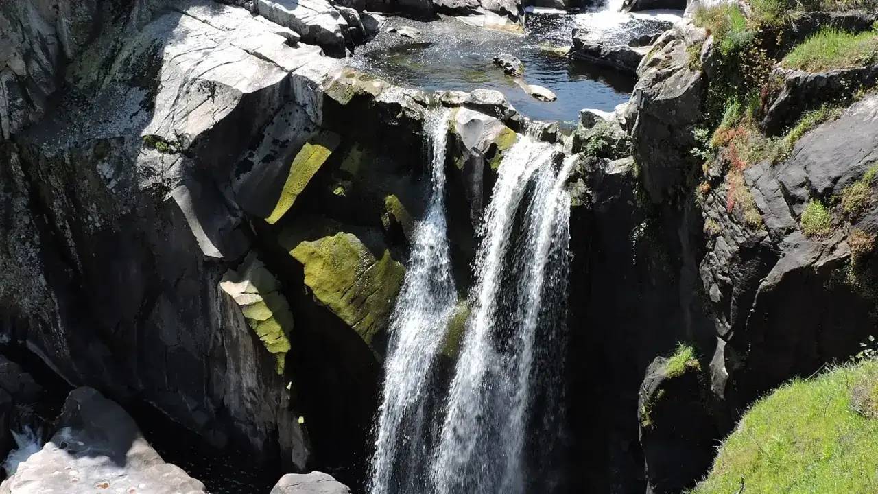 Cascada en el **pozo de los humos**, con rocas oscuras cubiertas de musgo verde y agua cayendo en cortinas blancas.