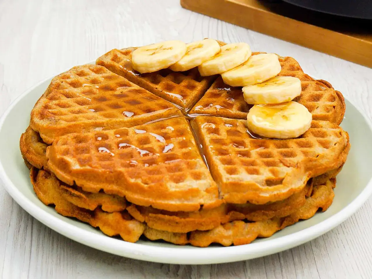Ein Stapel goldbrauner Waffeln, geschnitten und mit Bananenscheiben und Sirup belegt. Diese Waffel ohne Zucker ist ein gesunder Genuss.