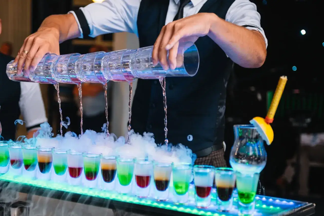 Barman nalewa kolorowe drinki na wesele do kieliszków, tworząc efektowny pokaz z dymem.