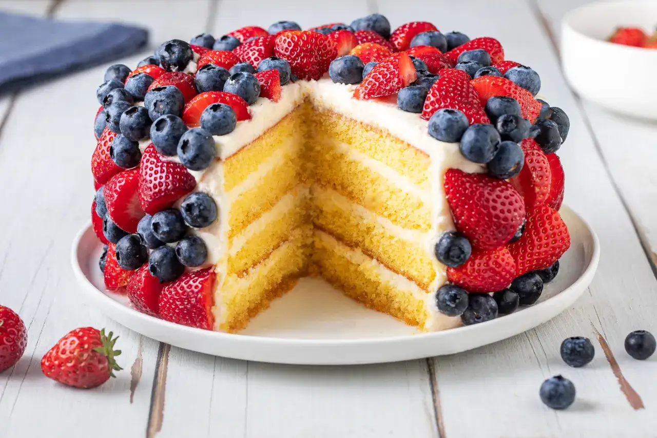Torta a pi&ugrave; strati con crema e decorata con fragole e mirtilli, un esempio di torte di compleanno particolari e fresche.