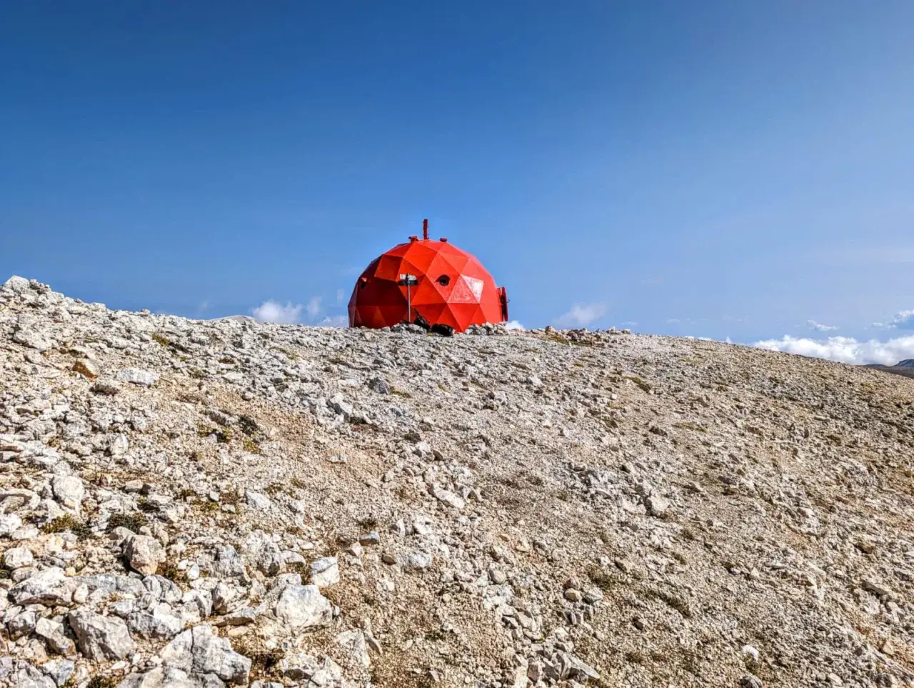 Rifugio rosso a forma di cupola su un pendio roccioso, meta di un'avventura di **monte amaro trekking**.