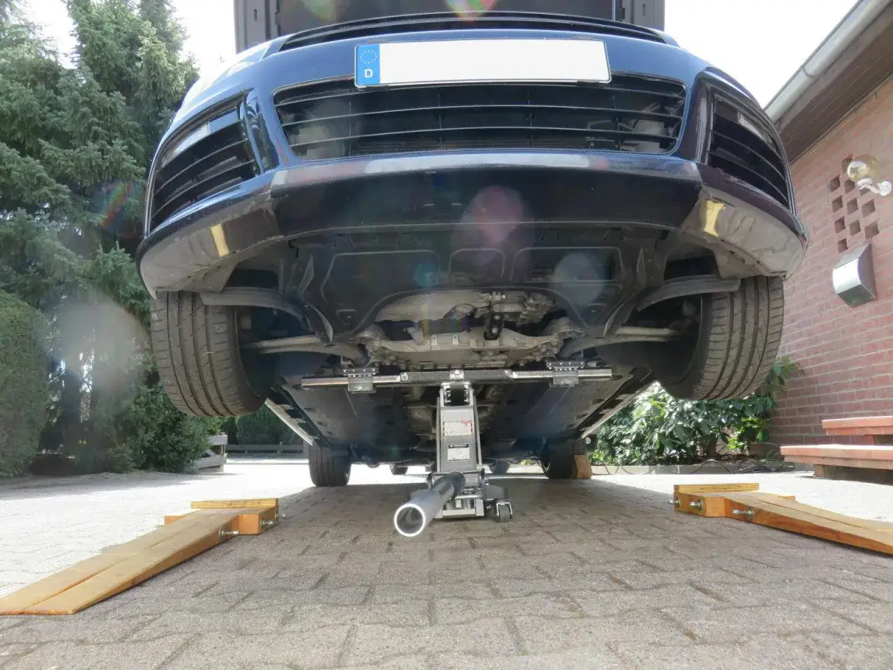 Auto wird mit Wagenheber aufgebockt, um darunter arbeiten zu k&ouml;nnen. Holzkeile sichern das Fahrzeug.