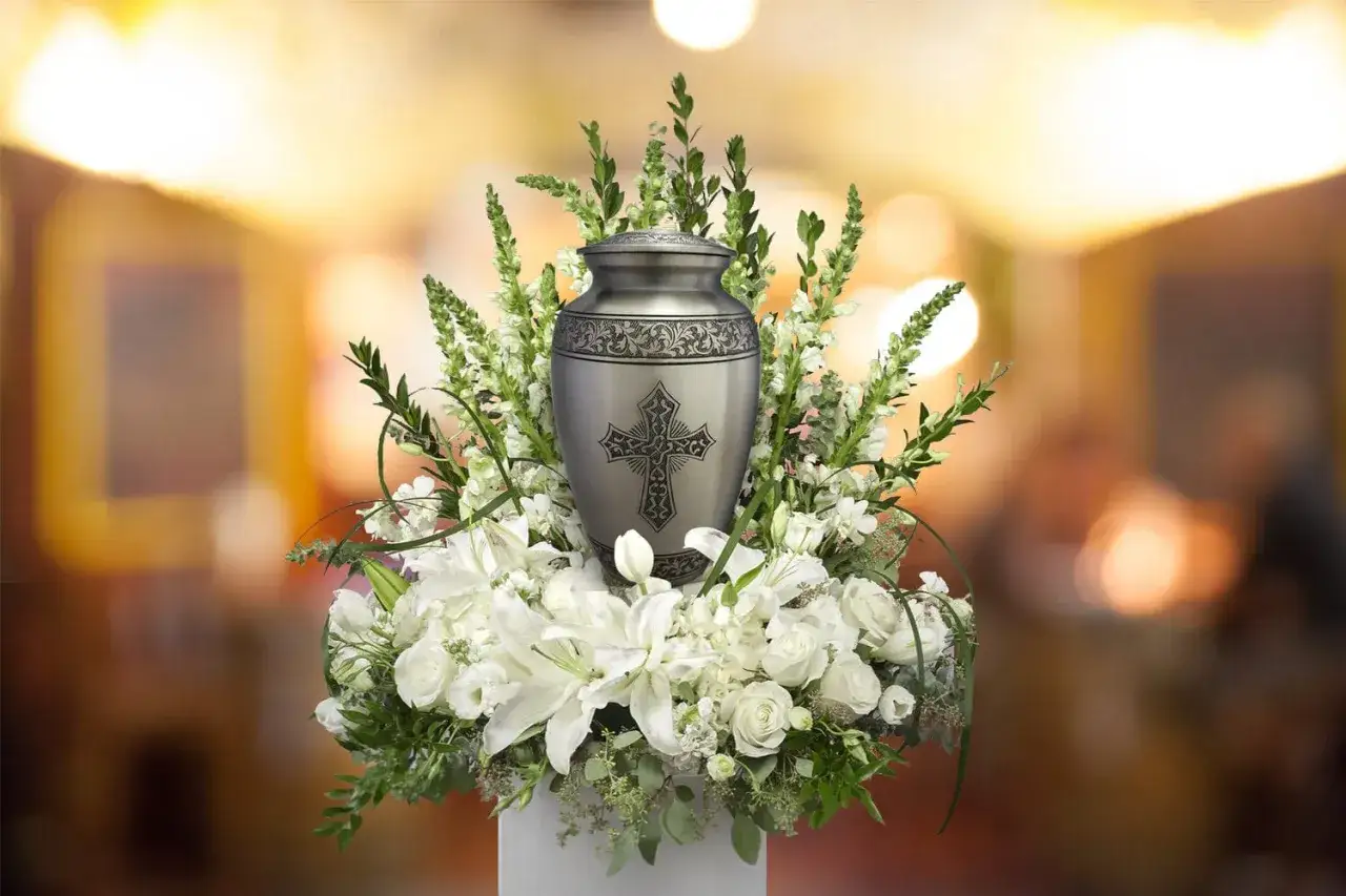 A cremation urn with a cross, surrounded by white flowers. The question 