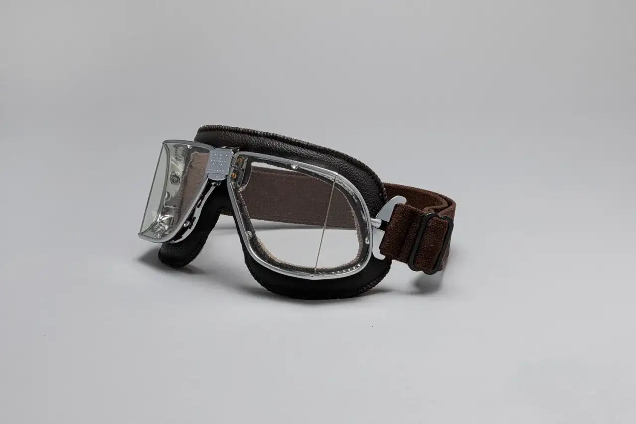 Occhiali biker in pelle marrone e metallo cromato, con lenti trasparenti. Perfetti per un look retrò.