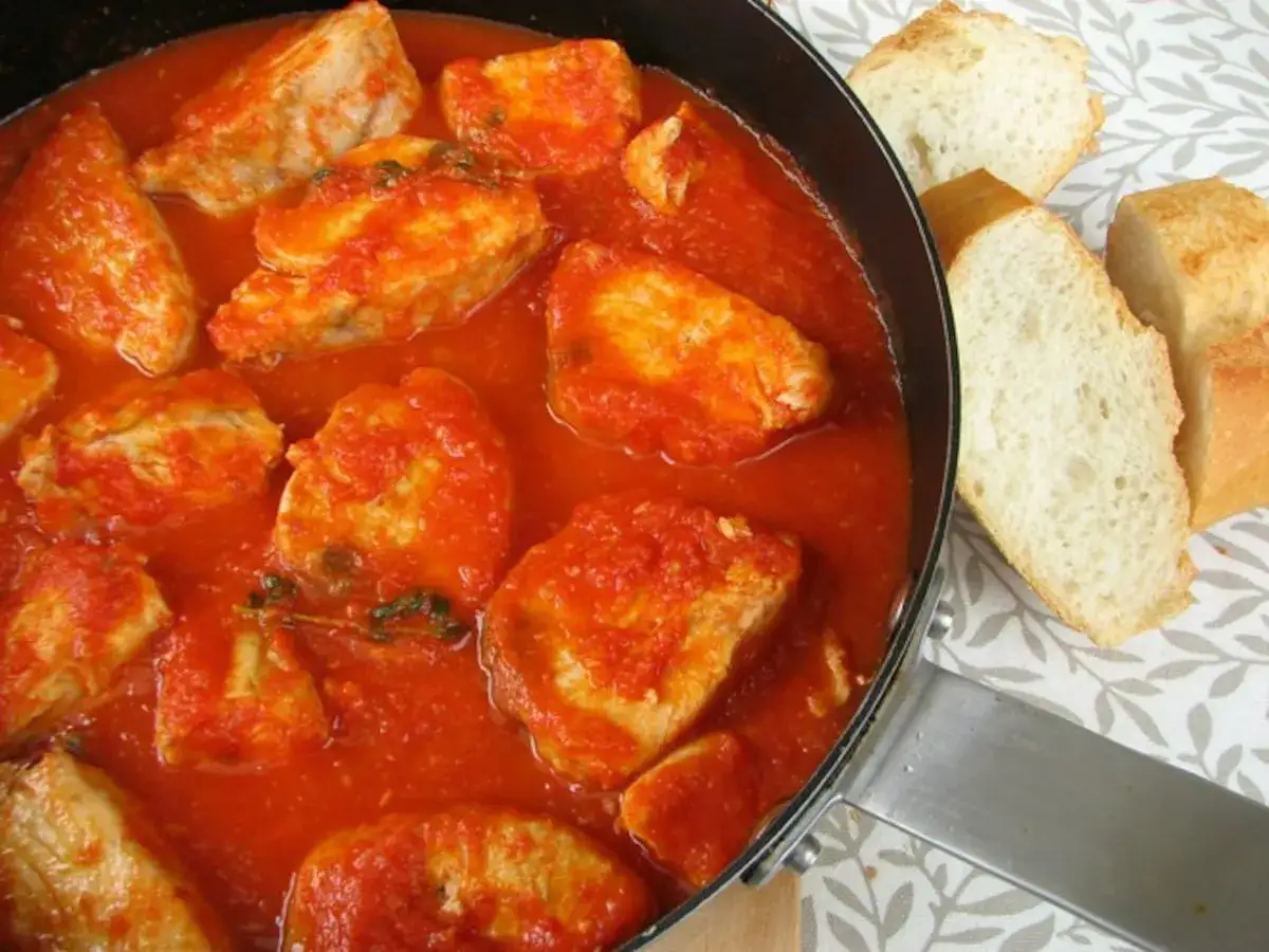 Un plato de pescado blanco en salsa de tomate, con trozos de pan crujiente al lado. Un bonito con tomate, listo para disfrutar.