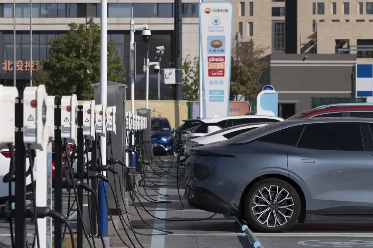 Auto elettrica con più autonomia in carica. Stazione di ricarica rapida con diverse colonnine e veicoli in attesa.
