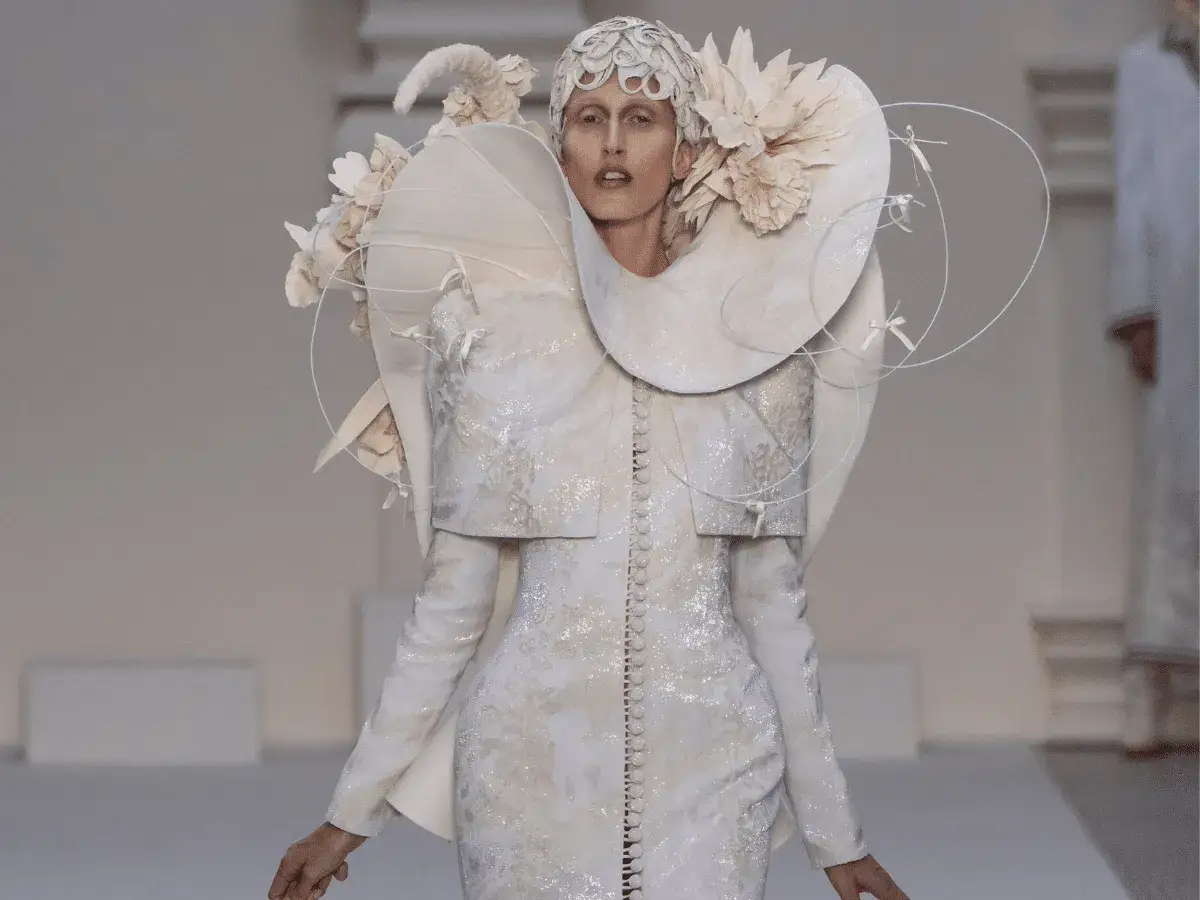 Modelka prezentuje kreację haute couture z białymi kwiatami i ozdobnym kołnierzem, przypominającą anioła.