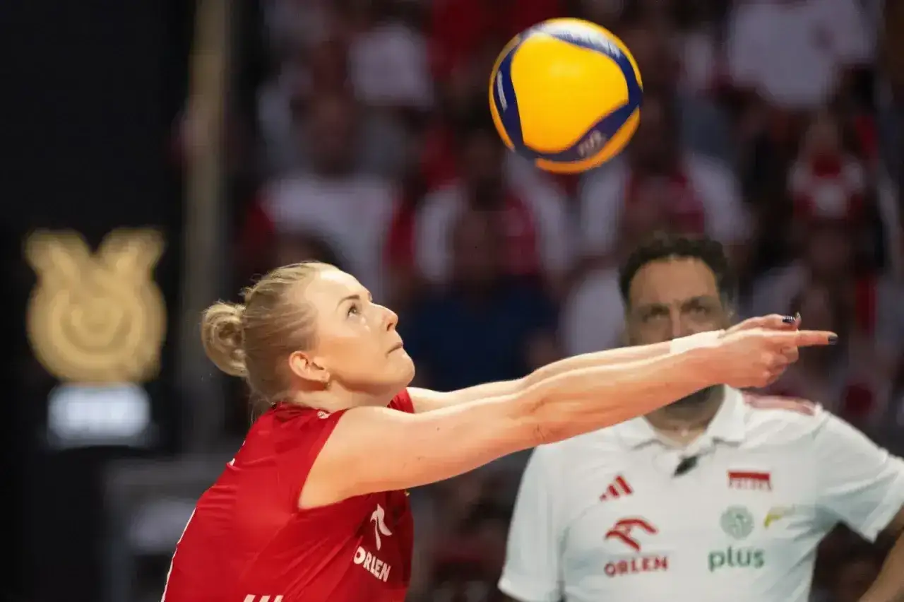 Joanna Wołosz, z mężem na trybunach, zagrywa piłkę do siatkówki.