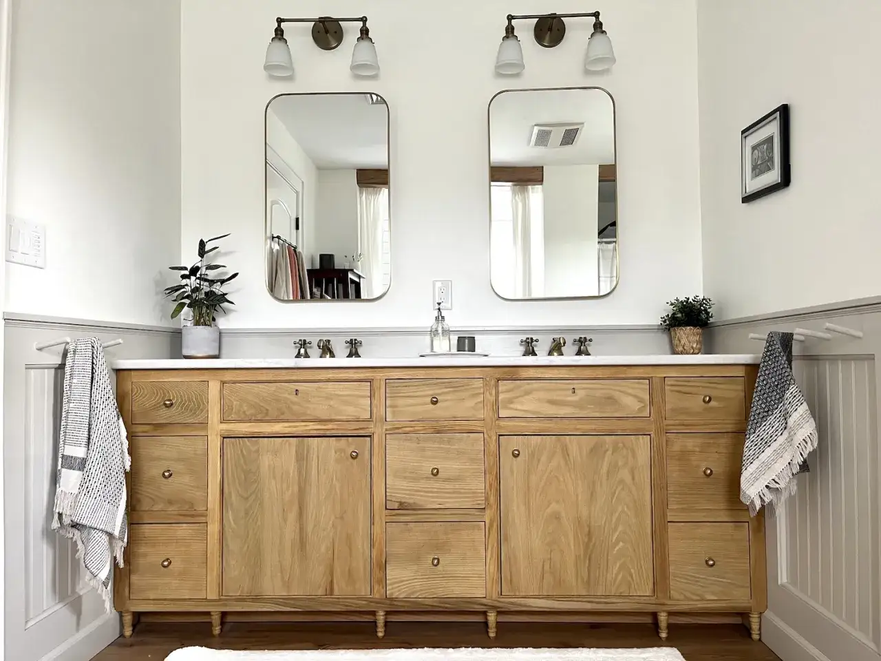 A beautiful DIY bathroom vanity with a natural wood finish, marble countertop, and brass fixtures. Two framed mirrors hang above, reflecting the bright, airy space.