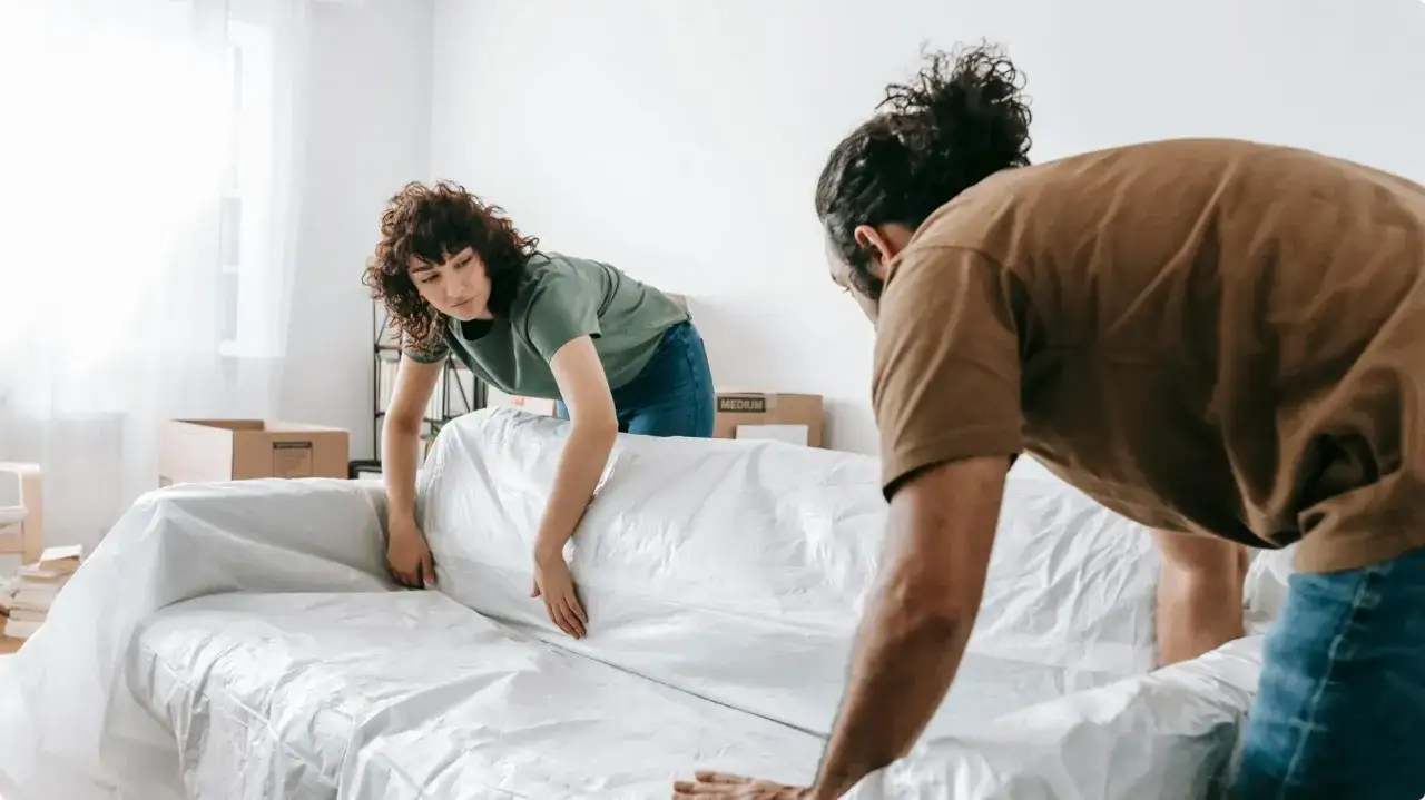 Un couple s'apprête à faire des travaux dans sa maison, protégeant leur canapé avec une housse en plastique.