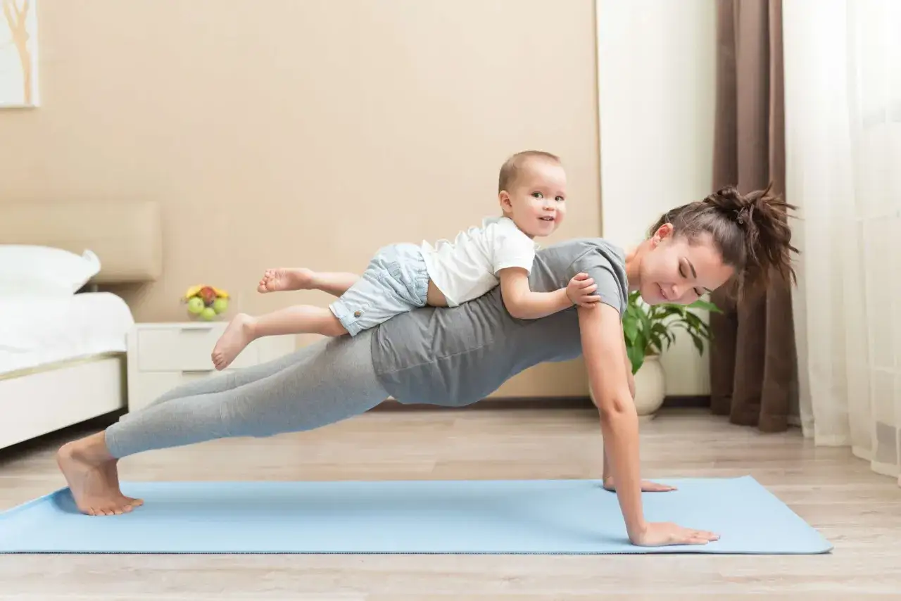 Mama na urlopie rodzicielskim 9 tygodni ćwiczy plank z dzieckiem na plecach.