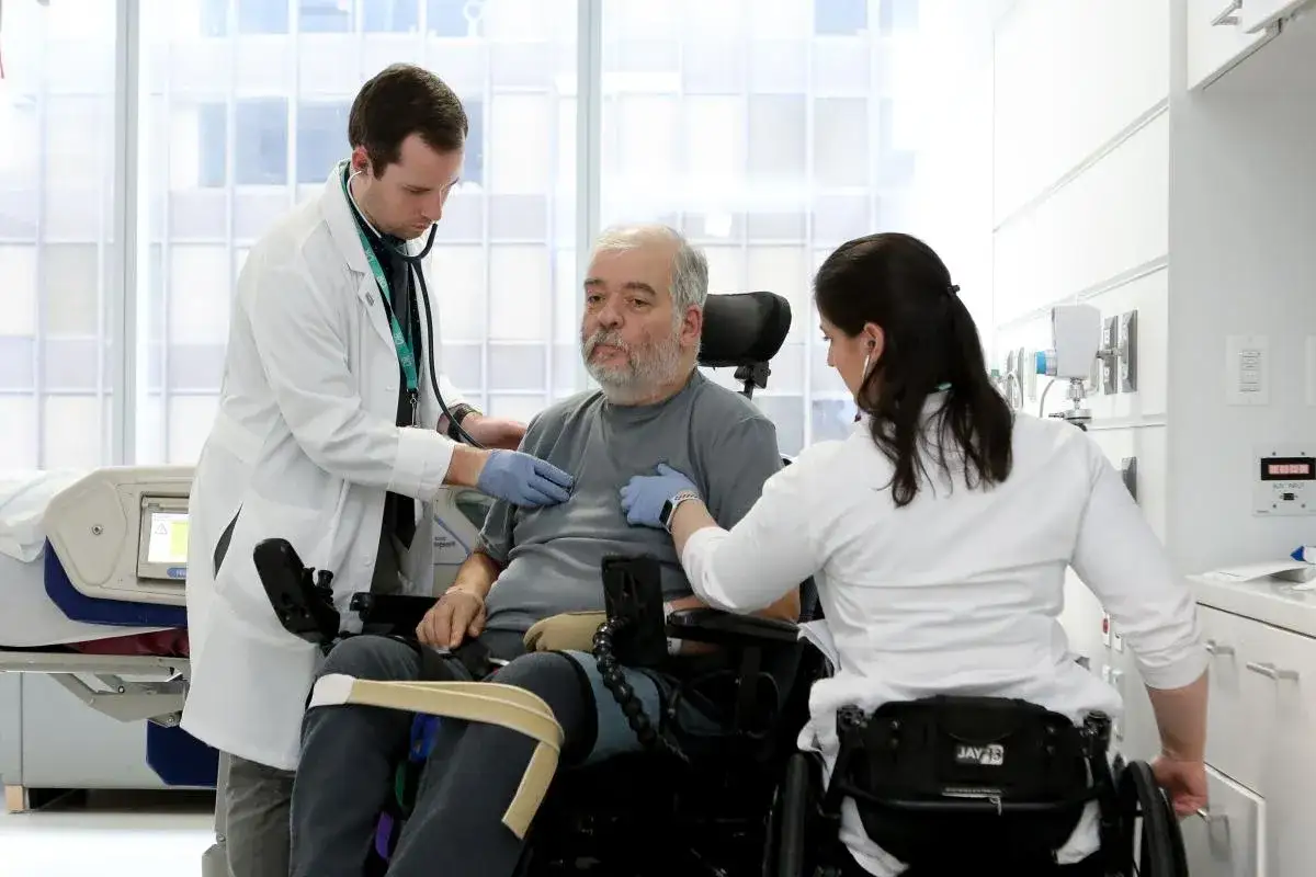 Un uomo in sedia a rotelle, affetto da sindrome locked-in, viene visitato da due medici.