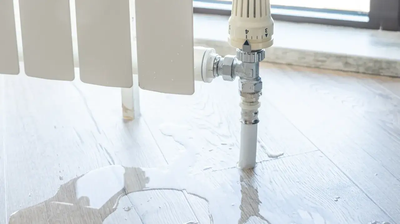 Radiador goteando agua. Una caldera pierde agua, es peligroso. El suelo de madera está mojado.