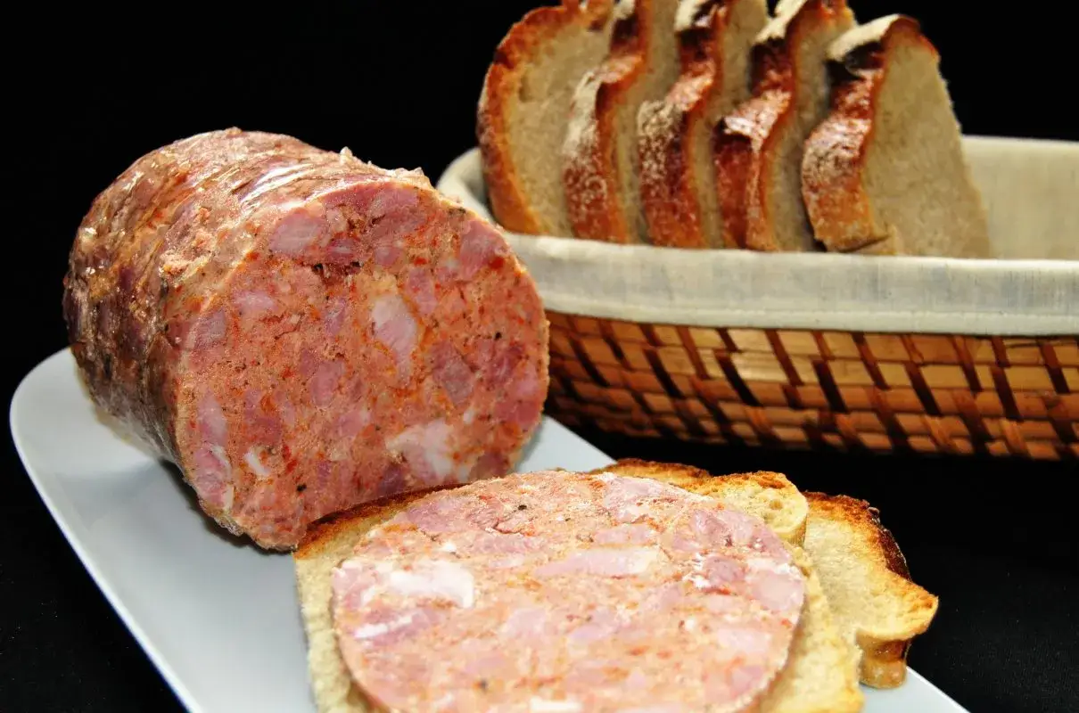 Pyszna łopatka z szynkowara na kromce chleba, obok koszyk z pieczywem.